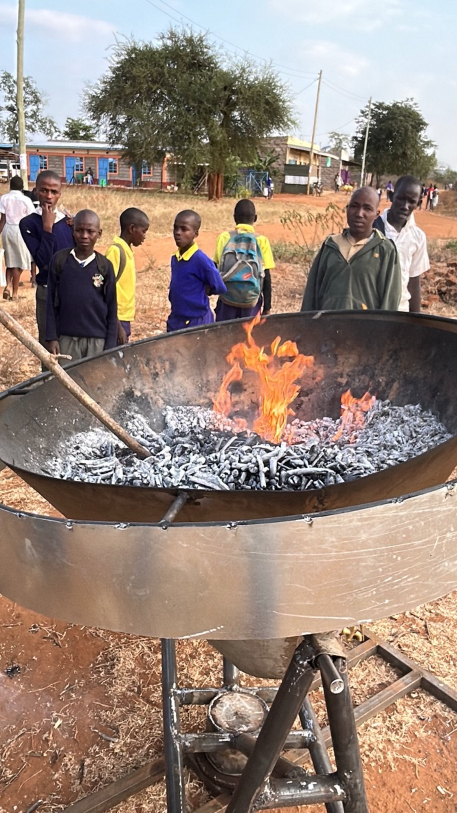 Glowing embers and forming biochar in the Kontiki kiln, with schoolchildren from the local community watching from the roadside.
